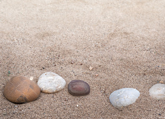 Fototapeta na wymiar Some sea pebbles in a row of curve line on sandy beach - five stones at soft blur background with copy space for marine concept or decoration in zen style.