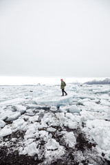 young male traveler in green clothes in a red hat and a green backpack stands on an iceberg on an ice lake in Iceland
