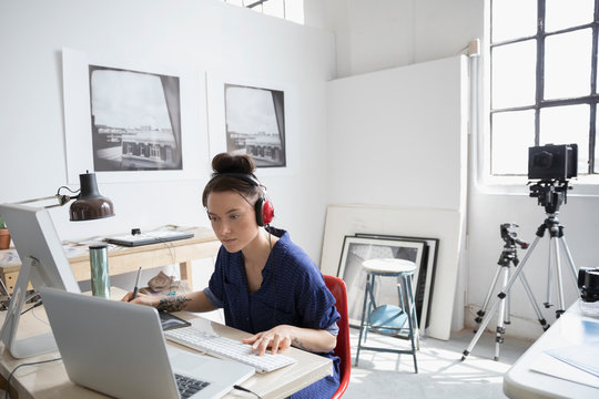 Female photographer with headphones working at laptop in art studio