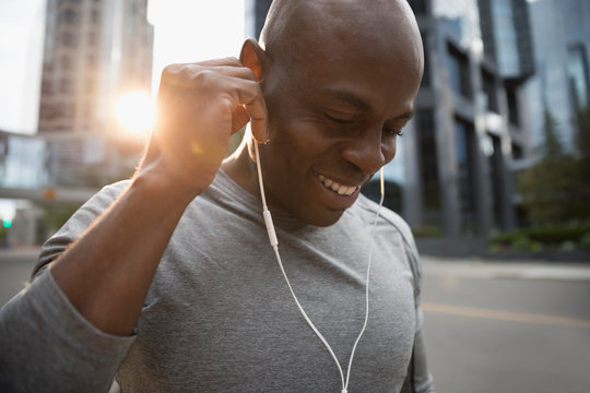 Close up smiling male runner listening to music with earbud headphones on urban street