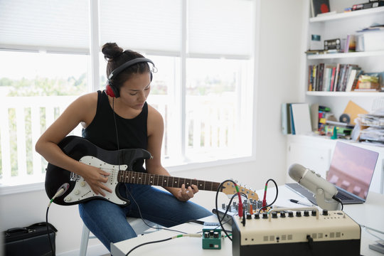 Teenage girl playing electric guitar, recording music at microphone in home office