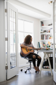 Teenage girl playing guitar in home office