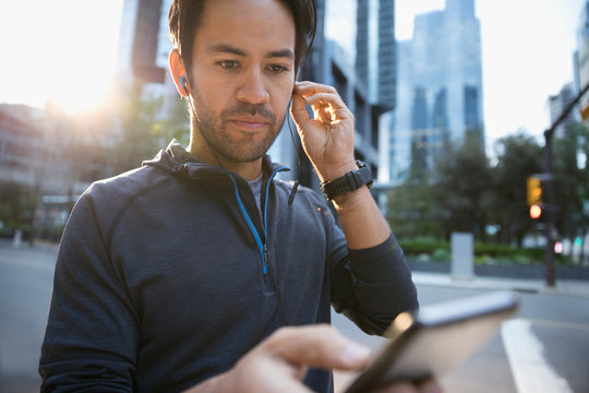 Male Runner Listening To Music With Earbud Headphones And Mp3 Player On Urban Street