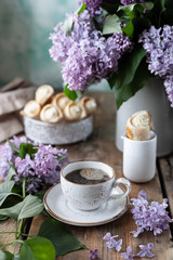 Obraz na płótnie Canvas Cup of coffee and cake horns from puff pastry with vanilla cream in a metal box in spring still life with a bouquet of lilacs on a wooden table