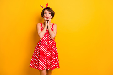 Photo of funny pretty lady hold arms on cheeks sending air kiss flirty mood wear retro summer dotted red white dress headband isolated bright yellow color background