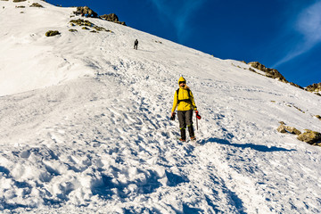 Winter mountain tourism. A tourist descending the summit on a well-trodden path in the snow on a slope.