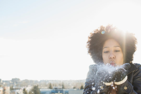 Woman blowing snow from hands against clear sky