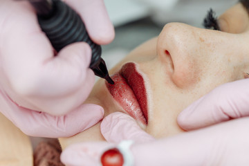 Woman having permanent makeup on lips in beauty salon - obrazy, fototapety, plakaty