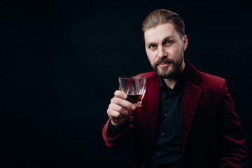 Stylish man in vinous jacket toasting with a glass of spirits in his hand isolated black background copyspace