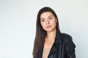 Obraz premium nice, beautiful serious girl is standing on gray background. Brunette in a black leather jacket. Natural portrait, natural makeup.