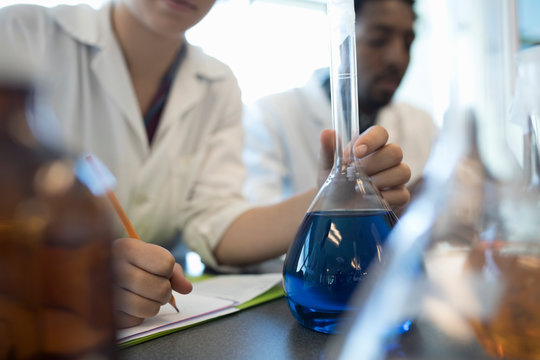 Close up male college student conducting scientific experiment, holding liquid beaker