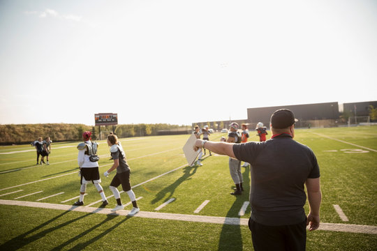Coach guiding high school football team practice on sunny football field