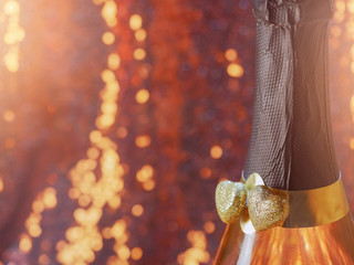 Two golden hearts covered with glitter on a champagne or sparking wine neck, Blurred bokeh background. Saint Valentine theme.