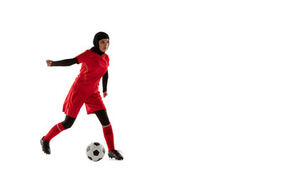 Fototapeta na wymiar Arabian female soccer or football player isolated on white studio background. Young woman kicking the ball, training in motion, action. Concept of sport, hobby, healthy lifestyle. Flyer, flysheet.