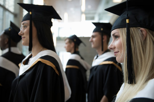 Confident female college student graduate in cap and gown looking away