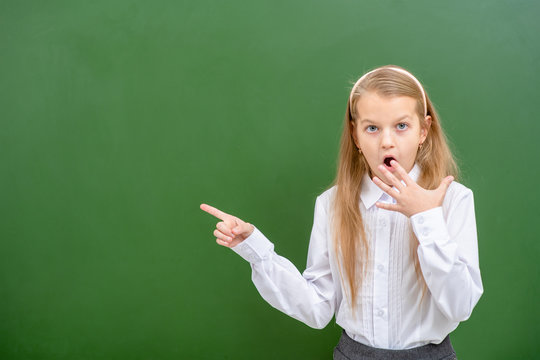 Shocked girl points on empty chalk board. Empty space for text