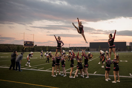Teenage girl high school cheerleading team cheering and jumping on sideline of game on football field