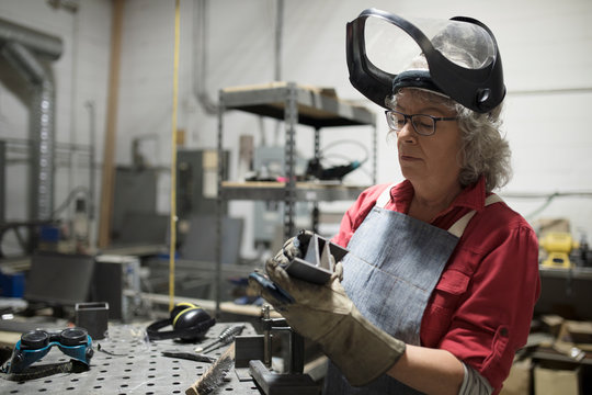 Senior female welder examining steel part in workshop