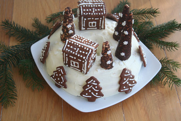 Chocolate cake covered by white cheese cream with decorated cookies in shape of little house on wooden table