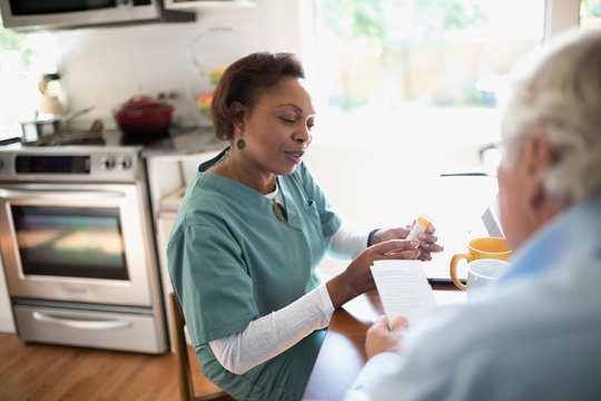 Smiling Home Nurse Explaining Prescription Medication To Senior Male Patient In Kitchen