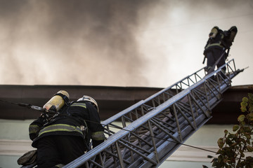 Firefighters on ladders in oxygen masks extinguish the fire in an old house in the middle of the...