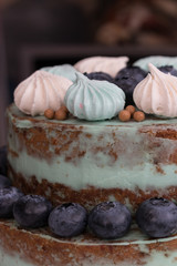 Homemade cake with brown cakes, green cream, decorated with colorful meringues and blueberries