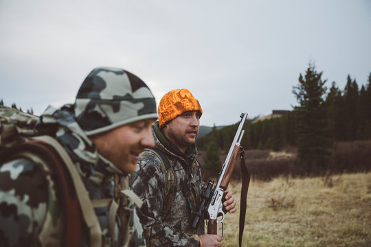 Male hunter friends in camouflage carrying hunting rifle in field