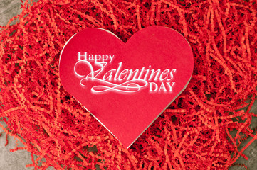 Holiday background for Valentine's Day on a gray cement background with red chopped wrapping paper and hearts.