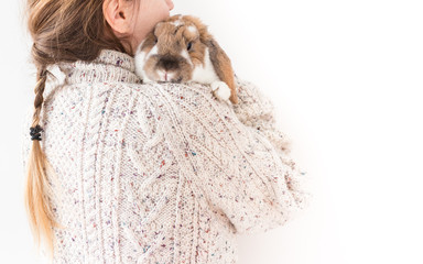 Girl in a thick sweater holding or hugging bunny, with empty copy space. Rabbit and a young woman or teenager isolated on white background studio shoot.