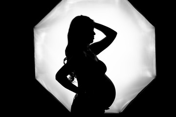 Beauty young pregnant woman black and white portrait. Beautiful Pregnant model girl posing in studio, touching her belly and smiling. Vertical photo, profile portrait. Healthy pregnancy concept