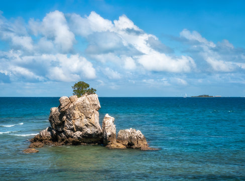 Sea stack at Rocher a la voile (Sailing Rock), historical landmark at Anse Vata Bay with Ile des Canards (Island of Ducks) in the background, in Noumea, New Caledonia,  South Pacific Ocean.