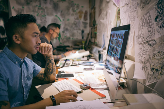 Tattoo Artist Viewing Digital Photographs On Computer In Tattoo Studio Office