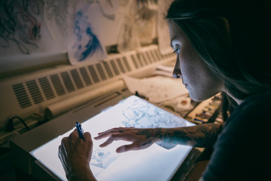 Tattoo Artist Sketching On Light Table In Dark Tattoo Studio Office