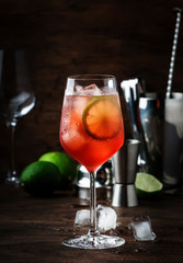 Campari tonic alcohol cocktail with red bitter, tonic, lime and ice. Old wooden table background,...