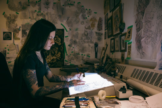 Tattoo Artist Sketching On Light Table In Dark Tattoo Studio Office