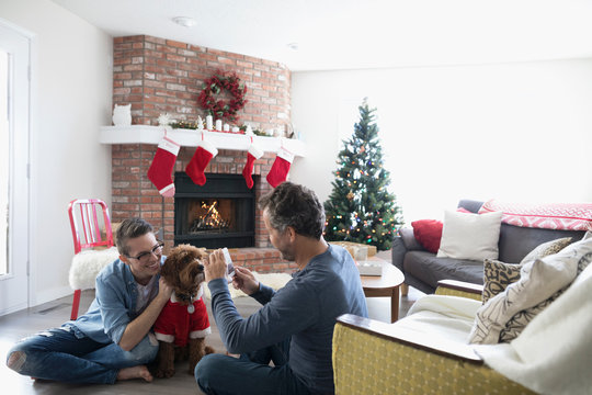 Father with smart phone photographing son and dog in Santa costume in Christmas living room
