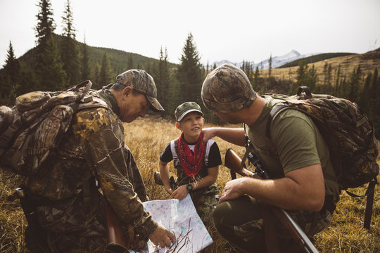 Multi-generation male hunters checking map in remote field