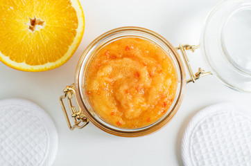 Homemade orange fruit facial mask (exfoliating sugar scrub) in the glass jar. Citrus DIY cosmetics and spa recipe. Top view, copy space.