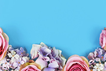 Background with artificial pink textile hydrangea and rose flowers at bottom and and blue blank copy space above