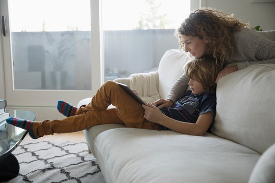 Mother watching son using digital tablet on living room sofa