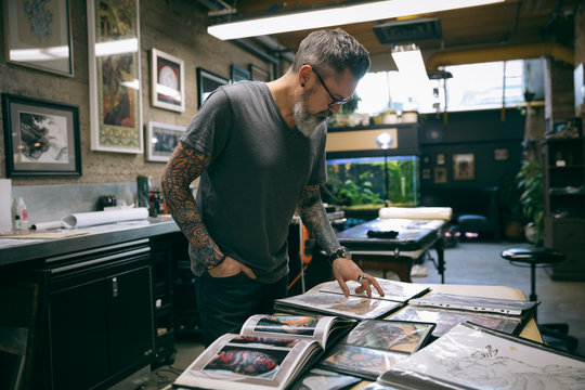 Tattoo Artist Reviewing Sketchbooks In Tattoo Studio