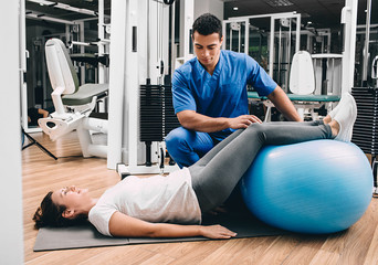 physiotherapist holds a fitness ball, helping the patient do exercises for the lower back. Lower back pain. Health Gymnastics