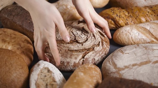A woman takes a loaf of bread from the table. Different types of whole grain bread served on the table