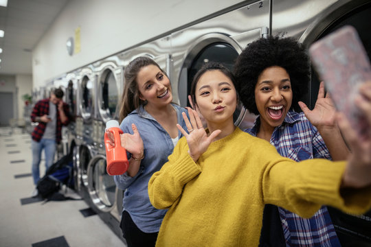 Playful young women friends posing for selfie while waiting for laundry at laundromat