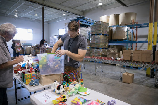 Male Volunteers Sorting Toys For Toy Drive In Warehouse