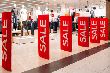 Red billboards stand at the entrance to a clothing boutique with sale information. In the background are manikins and hangers. Promotion, advertising, shopping and black friday concept