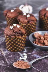 Homemade chocolate muffins with heart shaped sugar sprinkles in paper case with cup and spoon with cocoa powder on dark marbel background