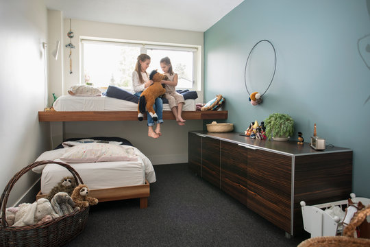 Sisters playing with stuffed animal on bunk bed in bedroom
