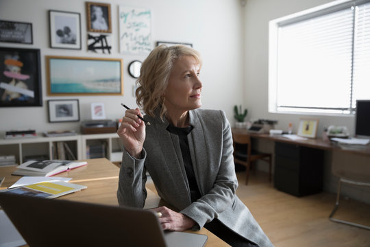 Thoughtful senior businesswoman entrepreneur working at laptop in studio office