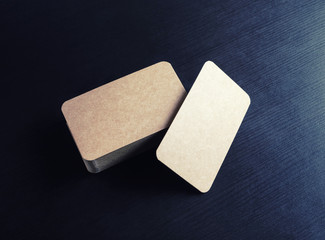 Blank brown paper business cards on black on black wooden background. Mockup for branding identity.